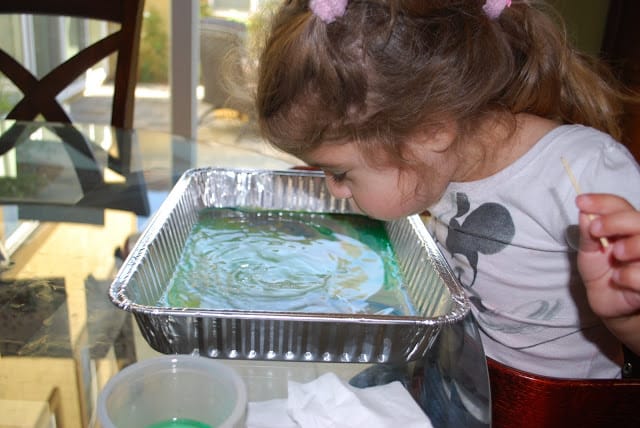 child blowing on colorful milk in tray