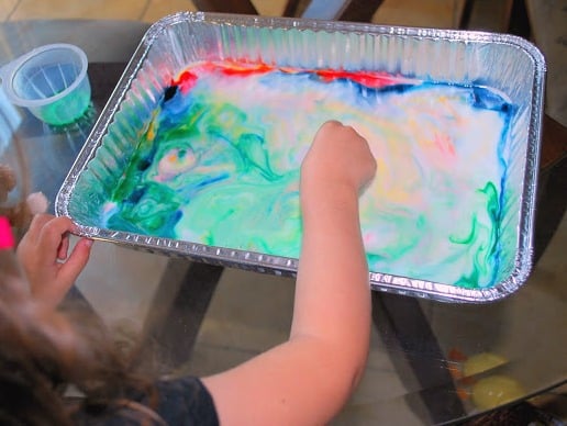 child playing with colorful milk in tray