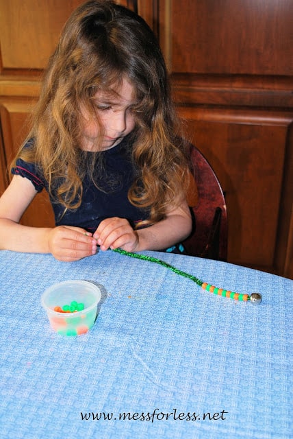 child putting beads on a pipe cleaner