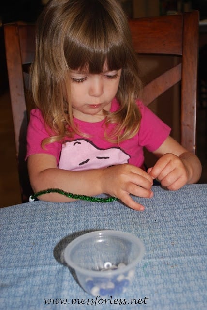 child putting beads on a pipe cleaner