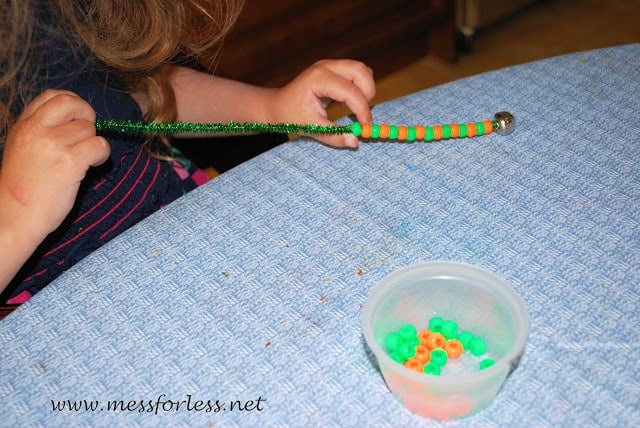 child putting beads on a pipe cleaner