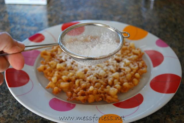 sprinkling powdered sugar on funnel cake