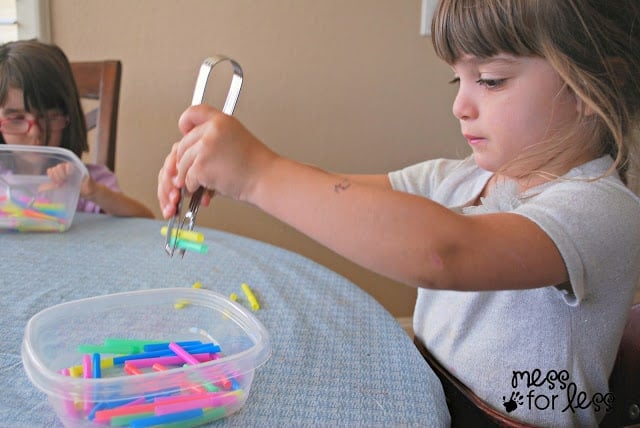 child picking up straws with tongs