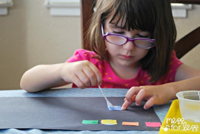 child gluing squares onto black paper