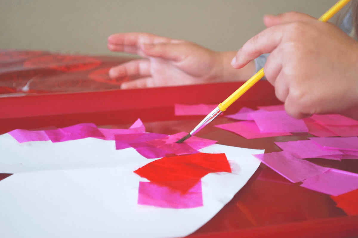 child painting tissue paper onto heart

