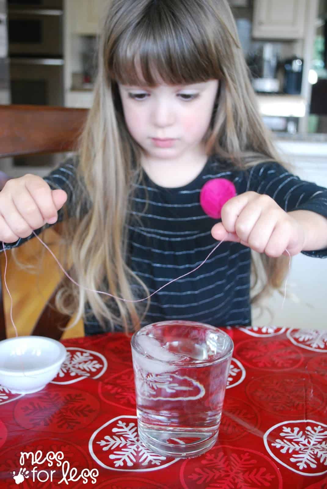 child holding a piece of thread over cup of ice