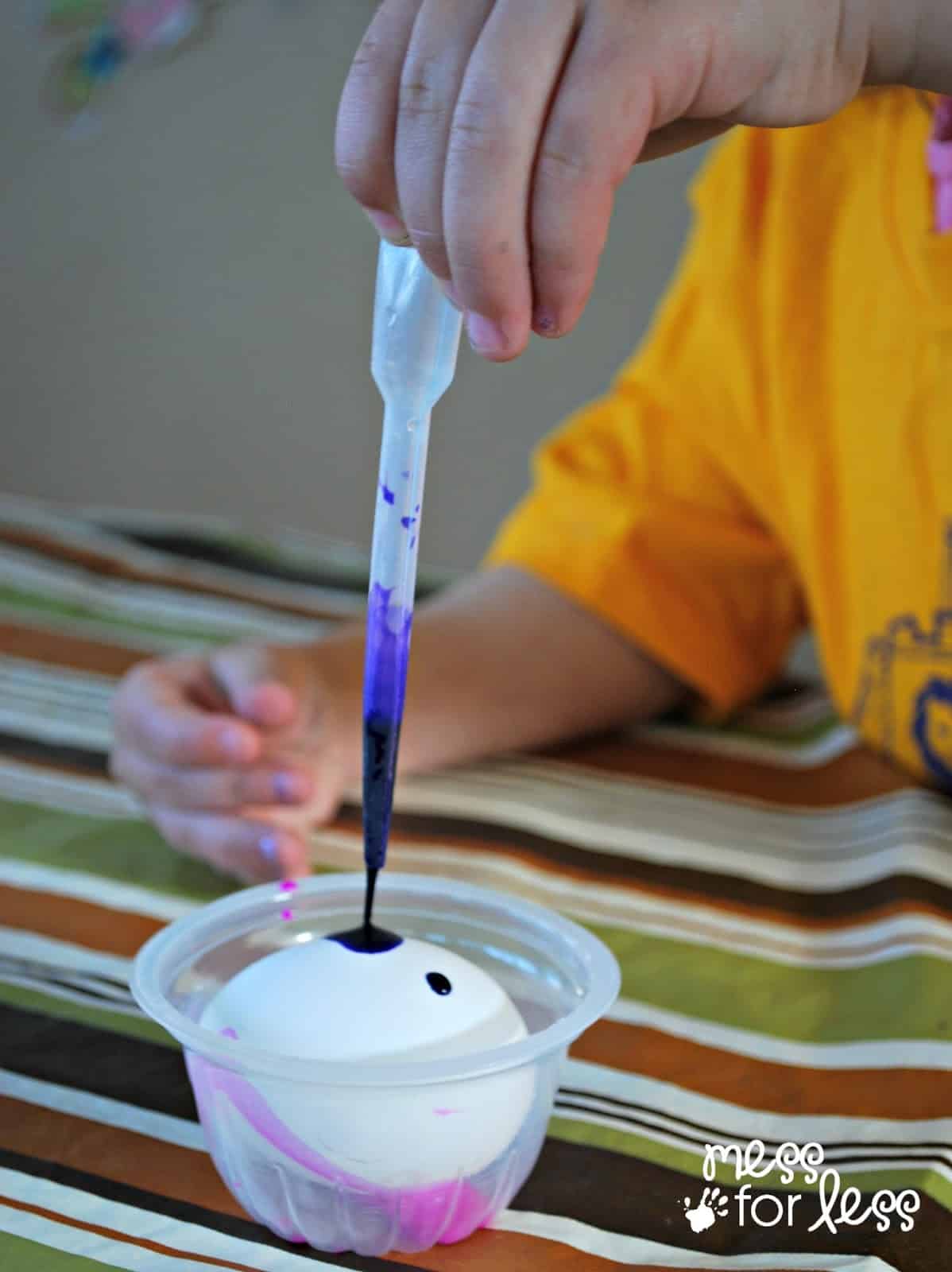 child dropping color with a dropper on egg.