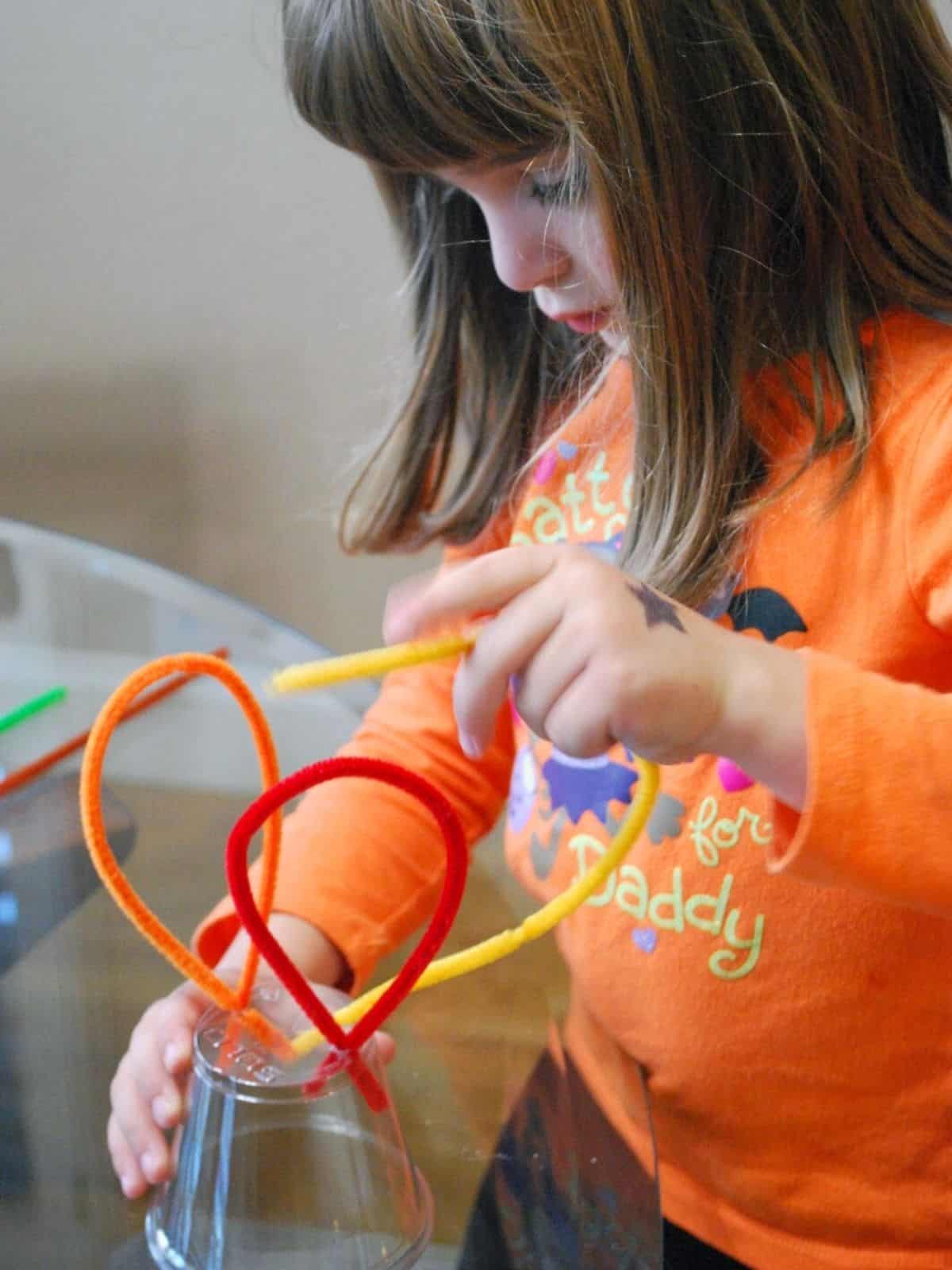 child placing pipe cleaners in holes in cup.