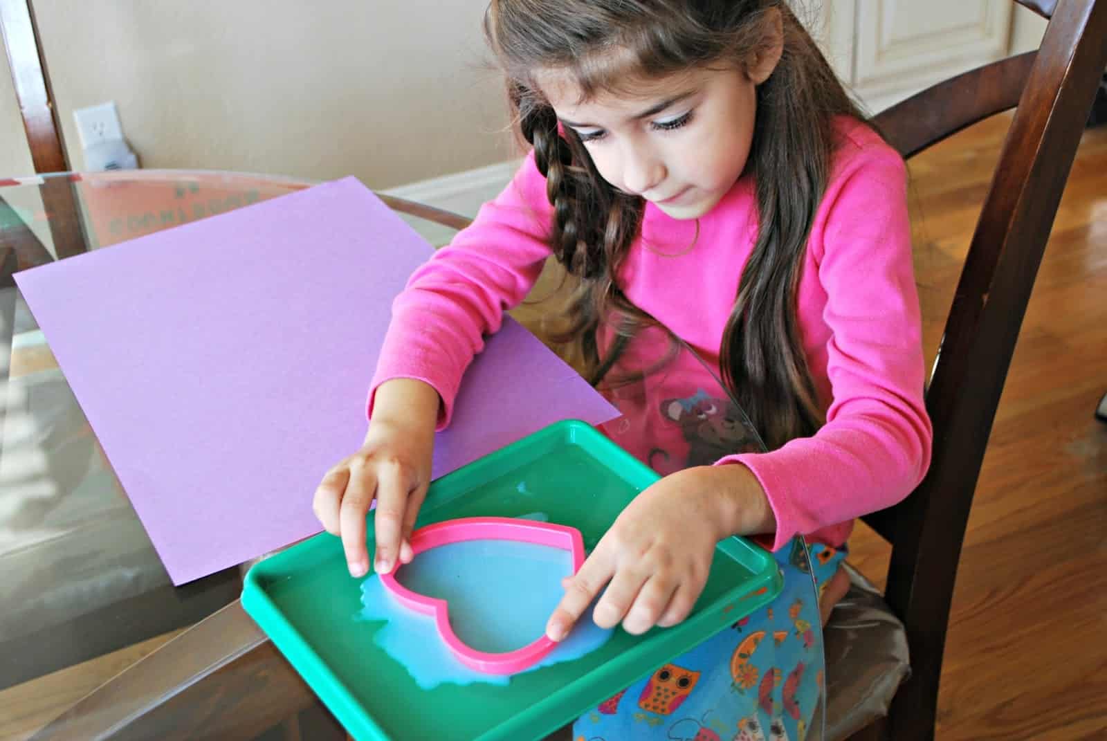 child placing a cookie cutter heart in glue