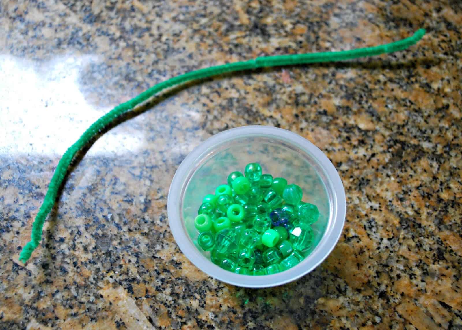 green beads in a bowl and a green pipe cleaner