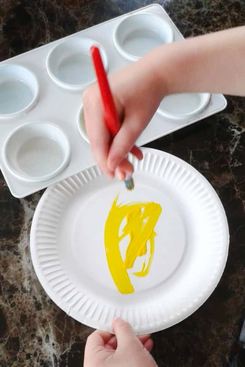 a hand with a paintbrush painting a paper plate yellow