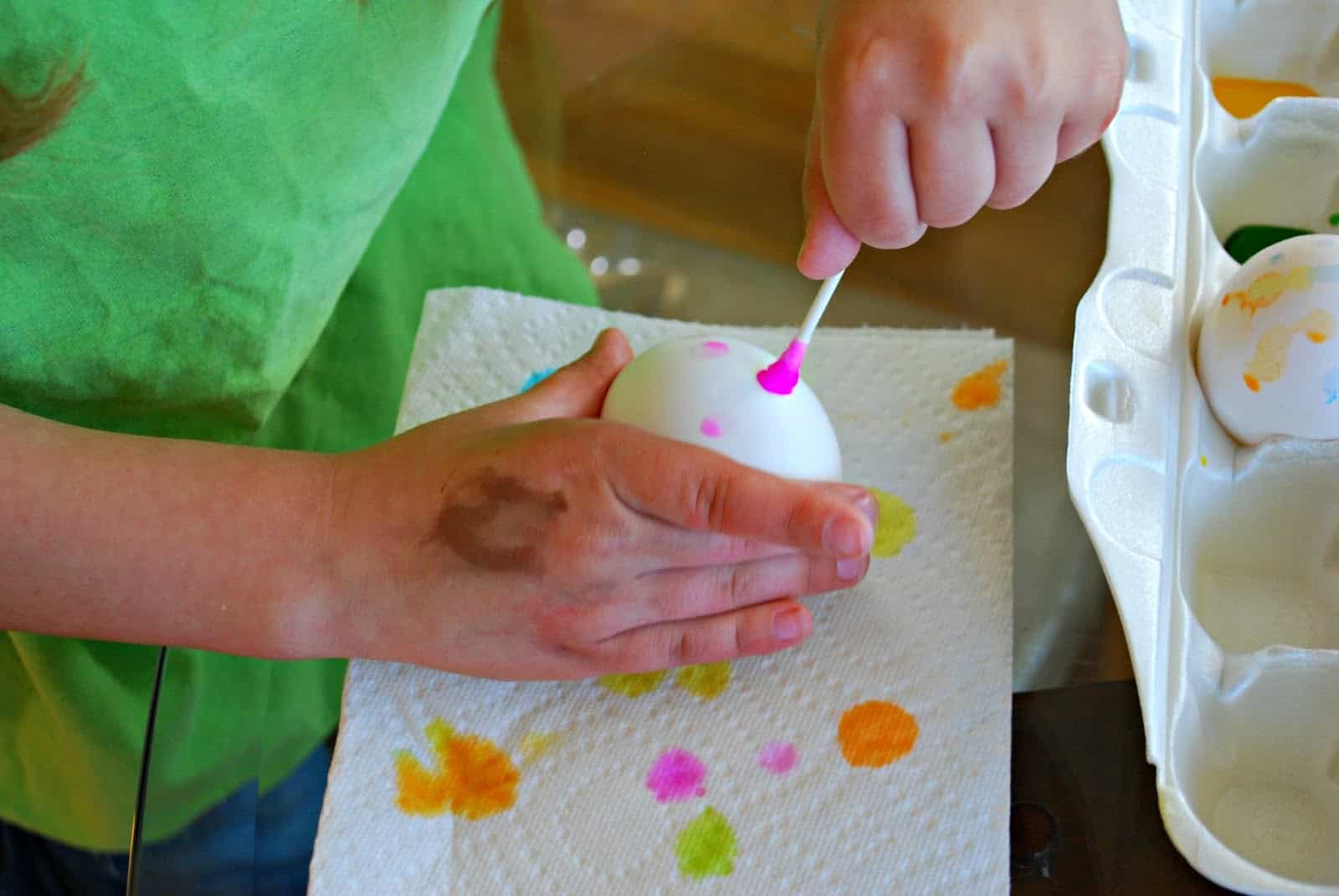 child holding egg and decorating with a q-tip