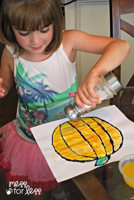 child shaking salt on pumpkin painting