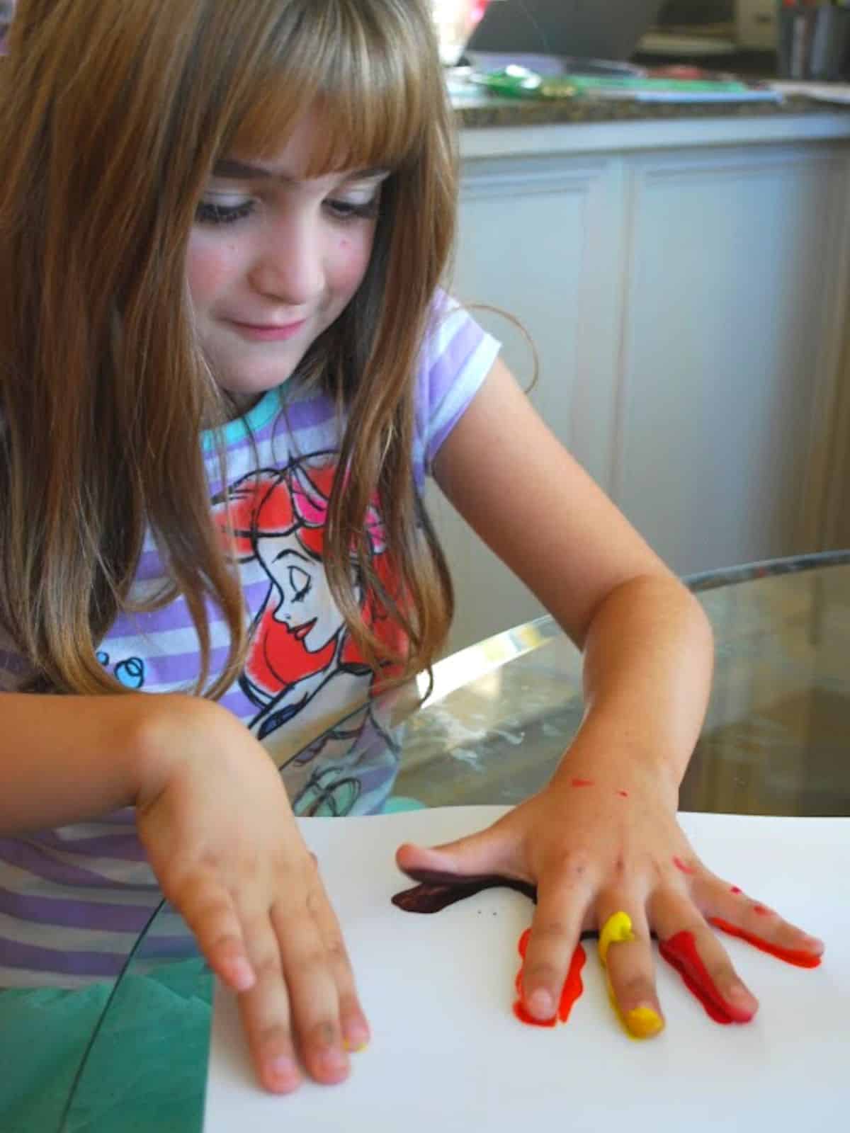 child making handprint with paint on white paper.