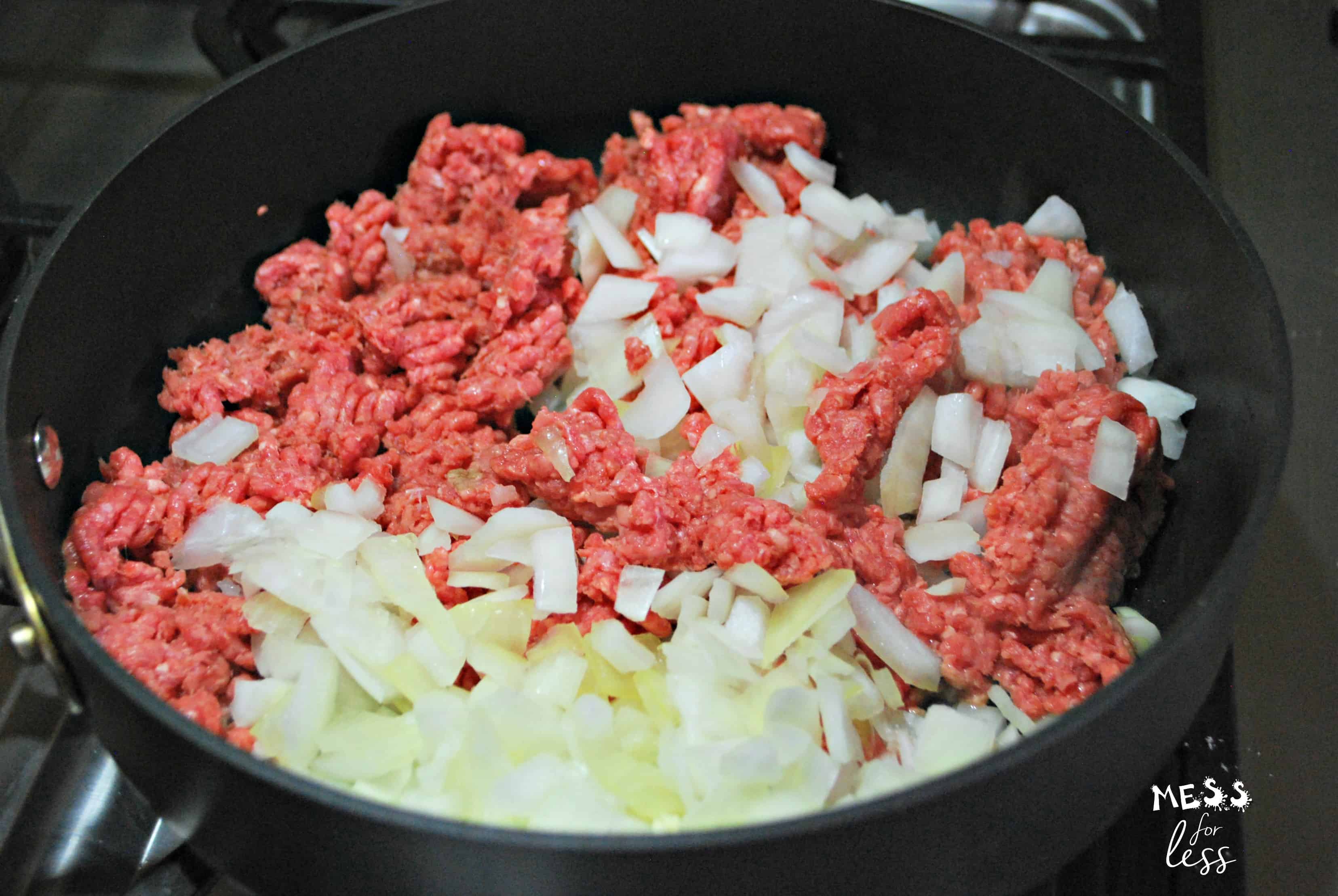 Ground beef and chopped onions cooking in a black skillet on a stovetop, the perfect start for a delicious hamburger tater tot casserole.