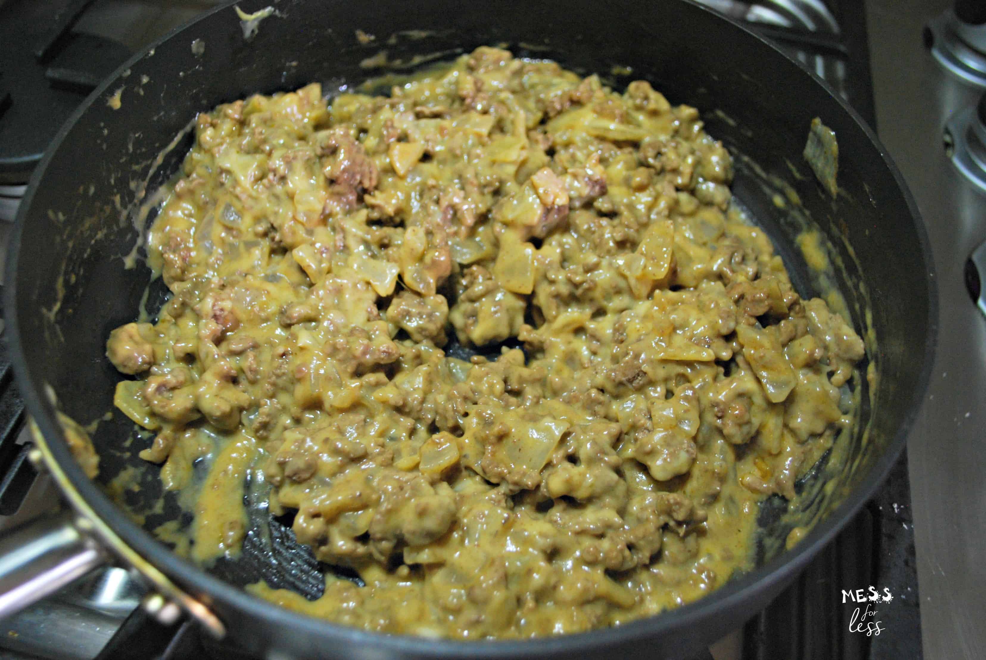 Ground beef and melted cheese mixture for a delicious hamburger tater tot casserole cooking in a black skillet on a stovetop.