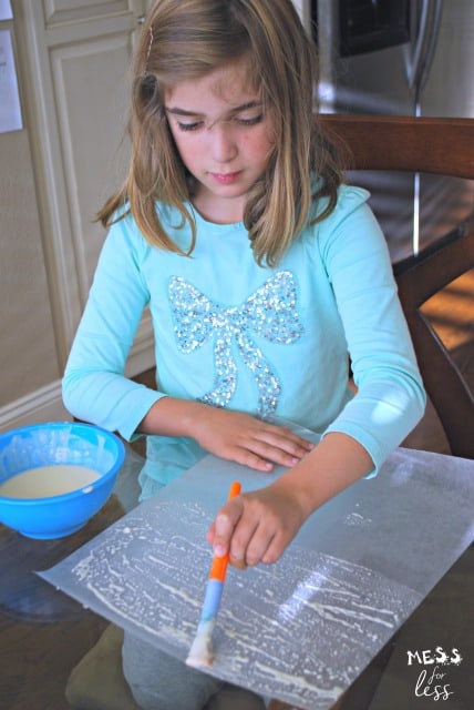 child brushing glue on wax paper