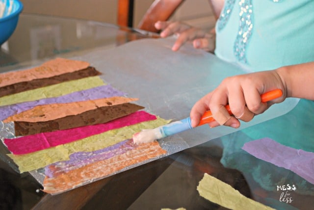 child painting glue on tissue paper strips
