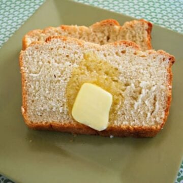 Two slices of bread from an easy bread recipe rest on a green plate, with a pat of butter melting on the top slice.