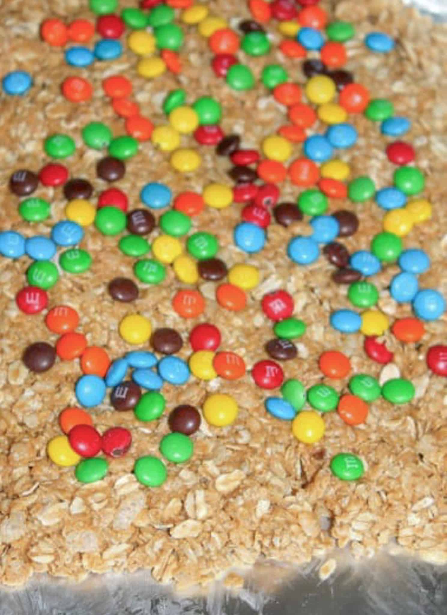 No bake granola bars topped with colorful mini M&M candies, arranged on a sheet of parchment paper for a fun and easy treat.