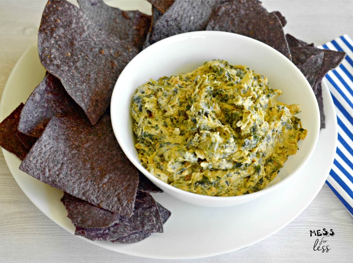 bowl of spinach artichoke dip surrounded by blue chips