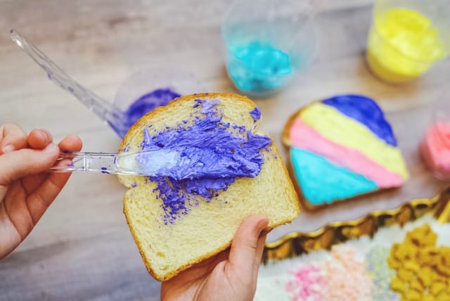 child spreading colored cream cheese on toast