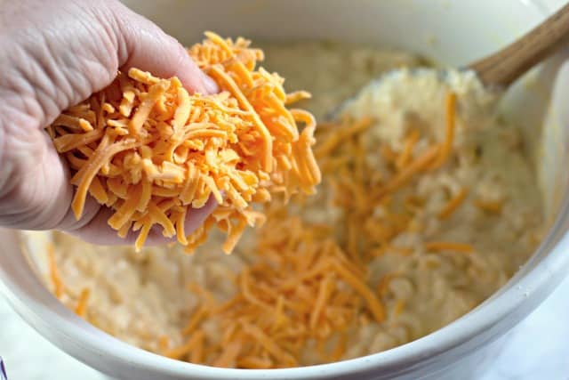 scooping shredded cheddar cheese into a bowl