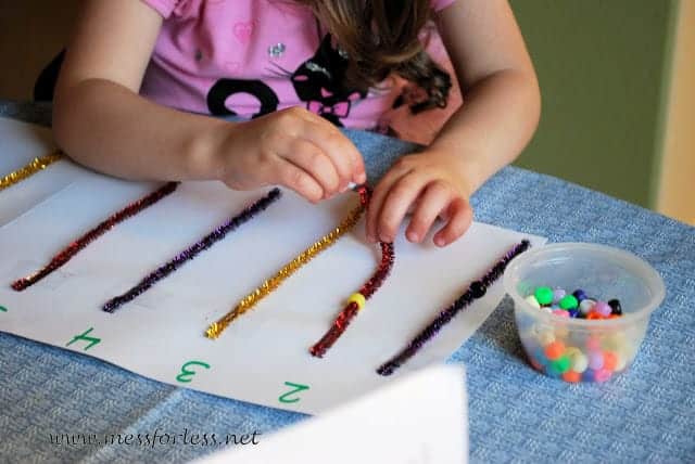 A child engages in fine motor activities for preschoolers by threading beads onto colored pipe cleaners spread across the table.