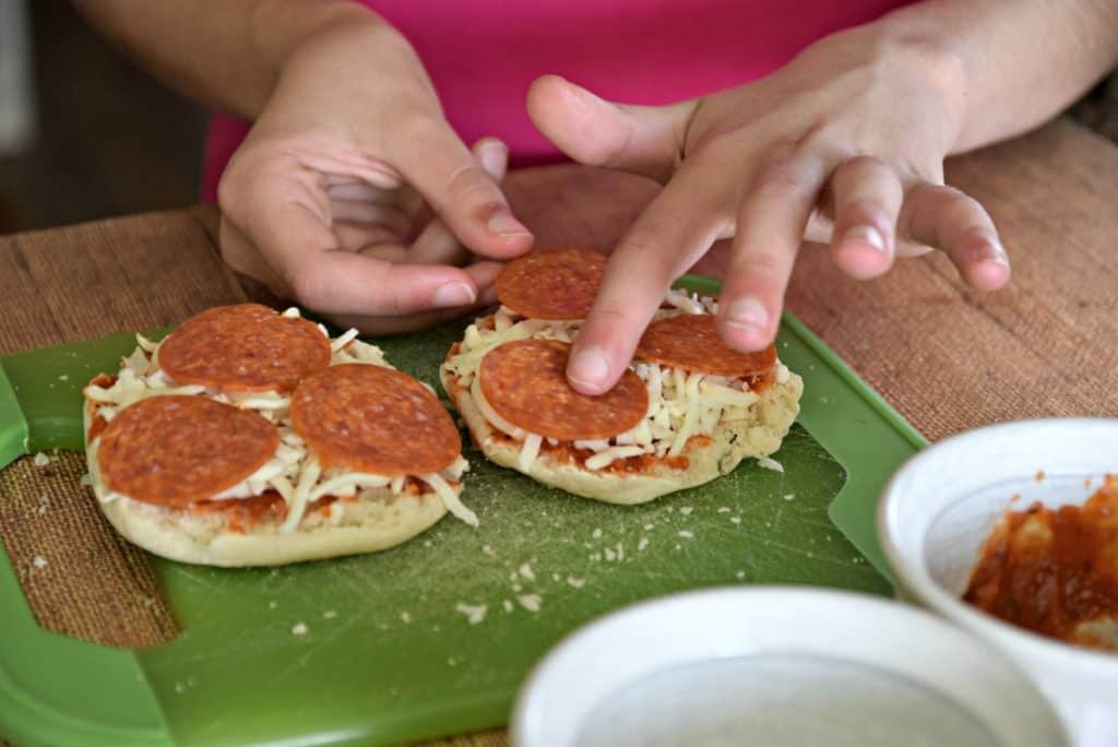 putting pepperoni on english muffin pizzas