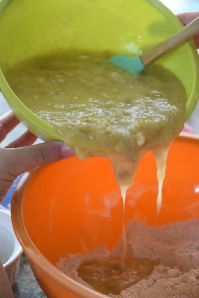 pouring mashed bananas into a bowl with dry ingredients