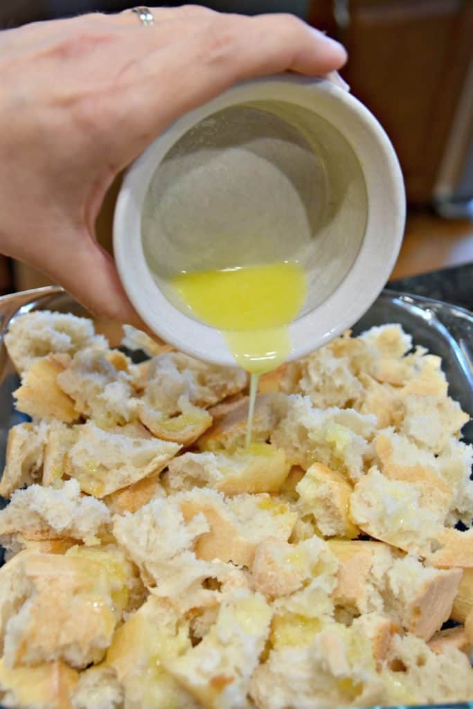 pouring butter on torn bread in a pan