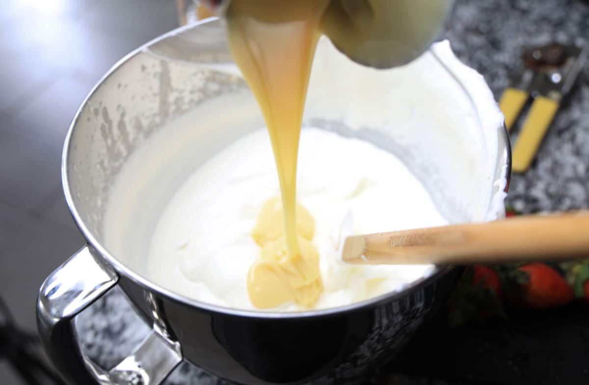 adding condensed milk to heavy cream in bowl