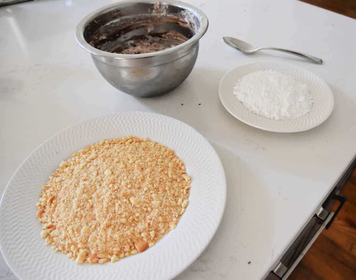 crushed wafers in plate, powdered sugar in plate and melted chocolate in bowl