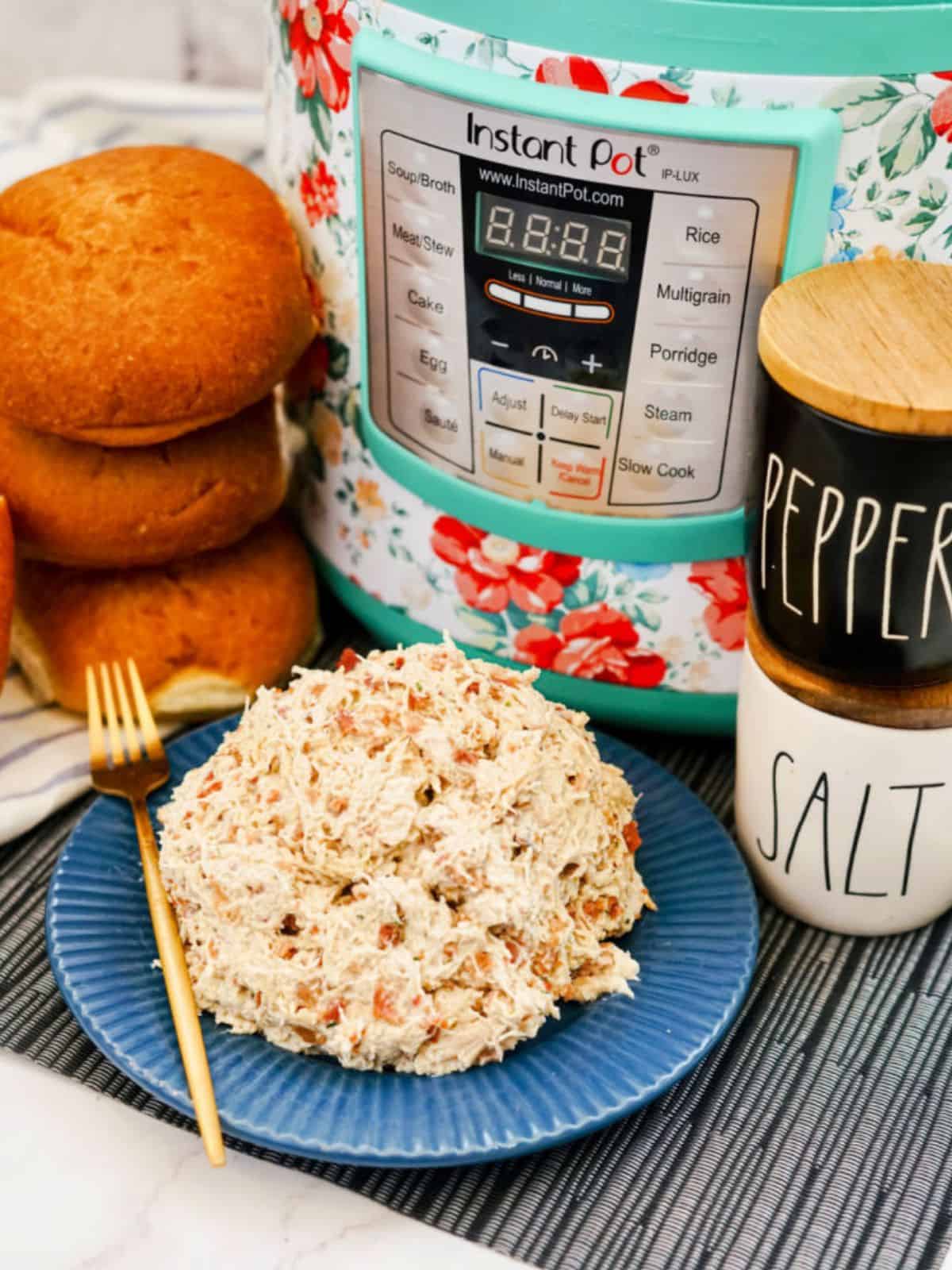 crack chicken on a blue plate with an instant pot in background and buns and salt and pepper