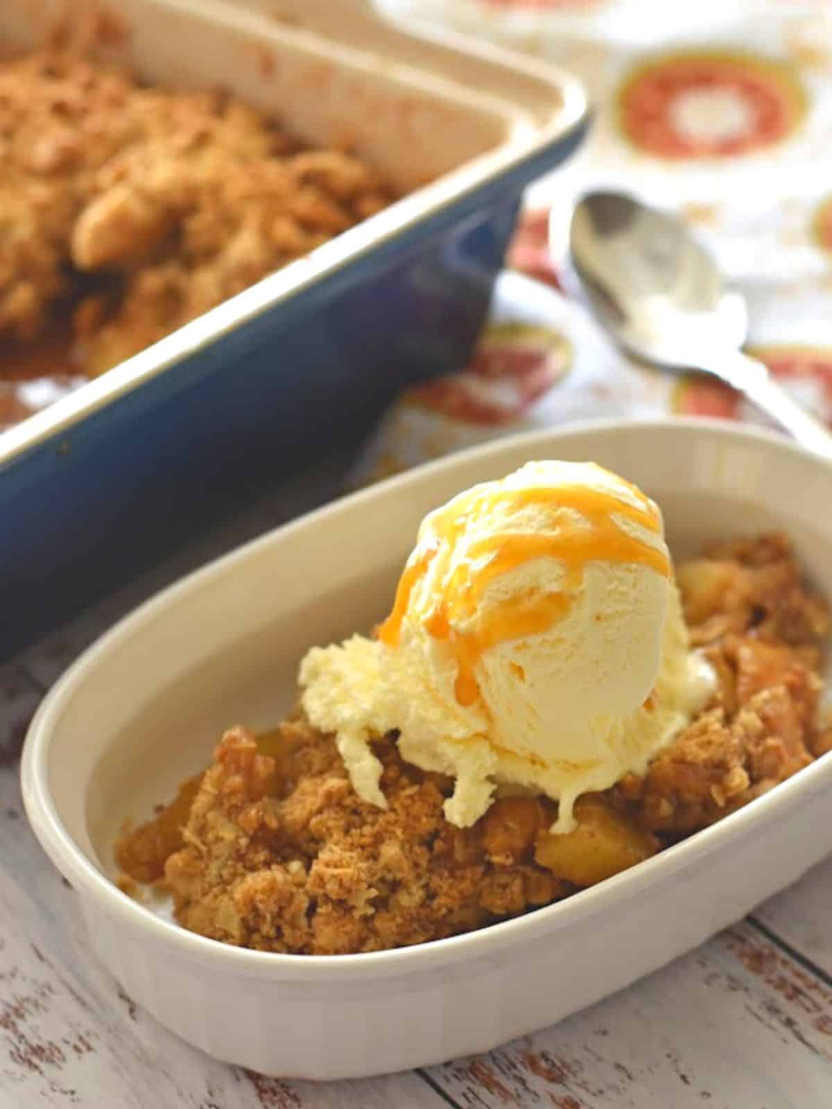 apple crisp in white bowl topped with vanilla ice cream