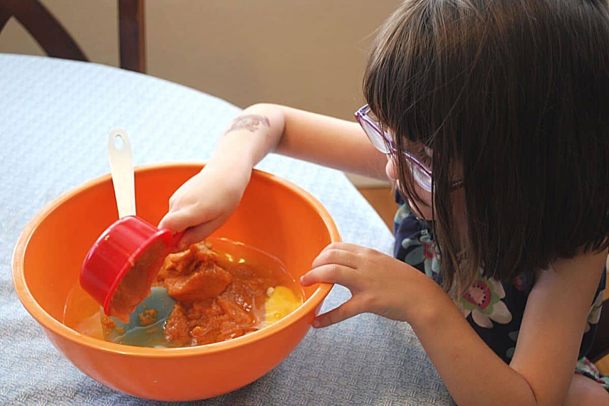 child pouring pumpkin puree in bowl