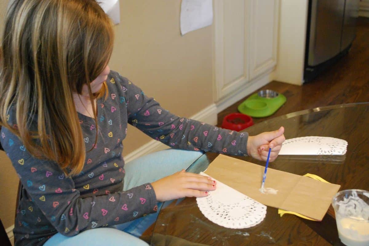 child placing glue on paper bag.