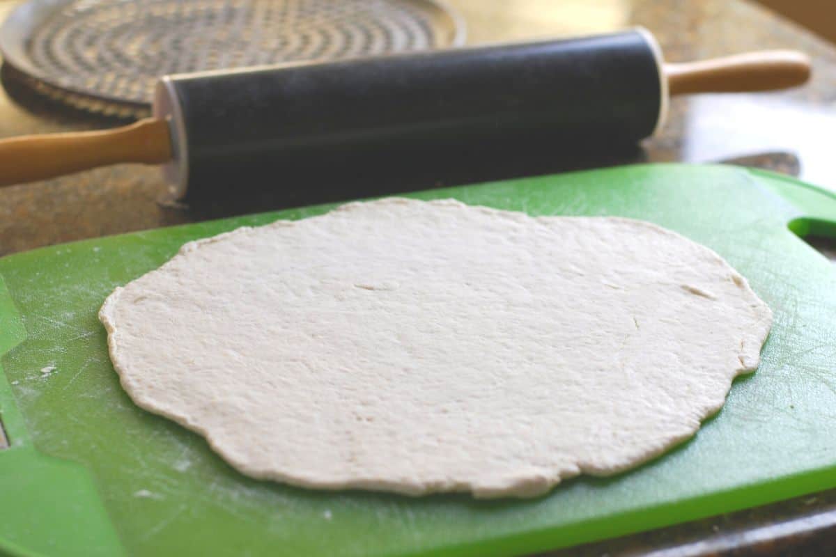 pizza dough rolled out on green cutting board