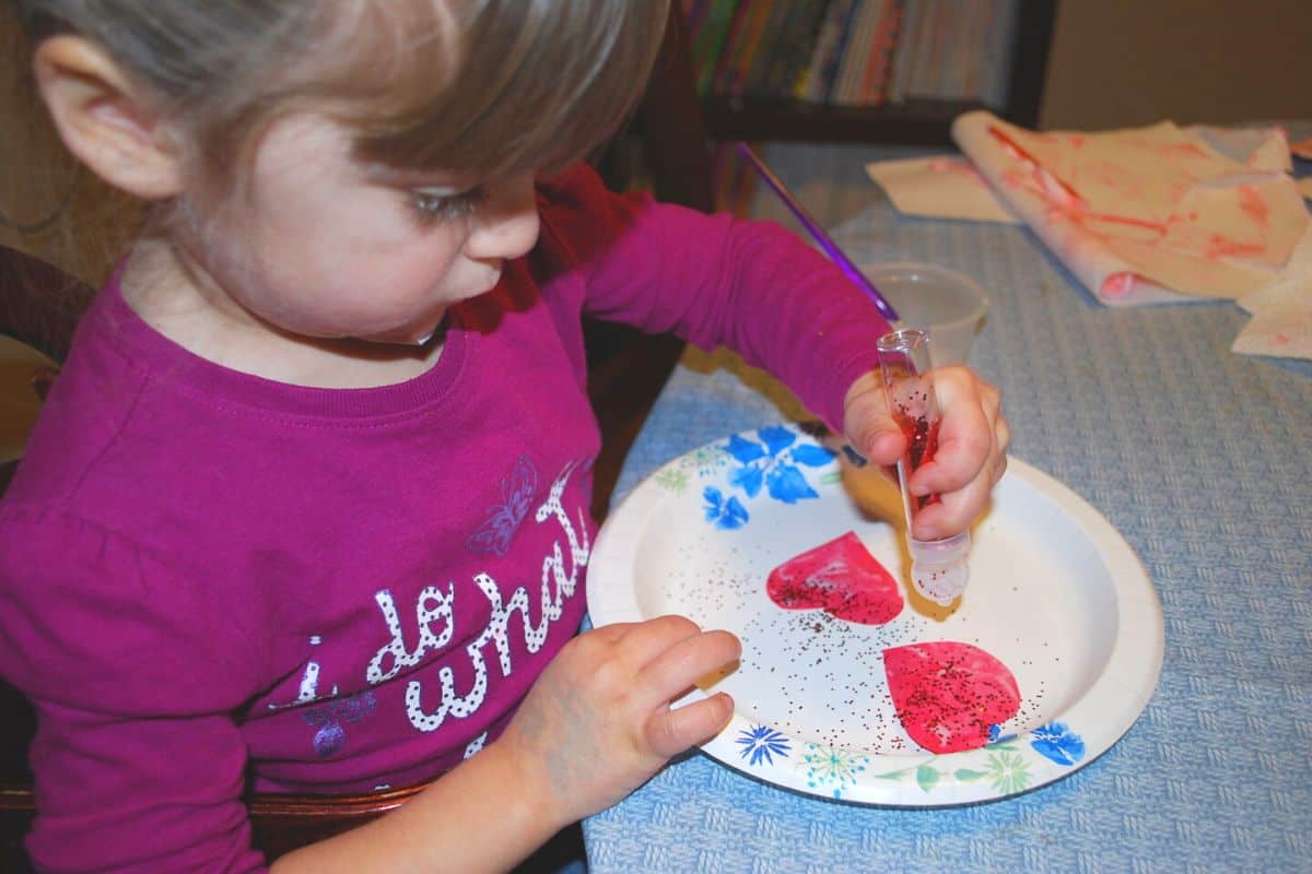 child sprinkling glitter on red paper heart