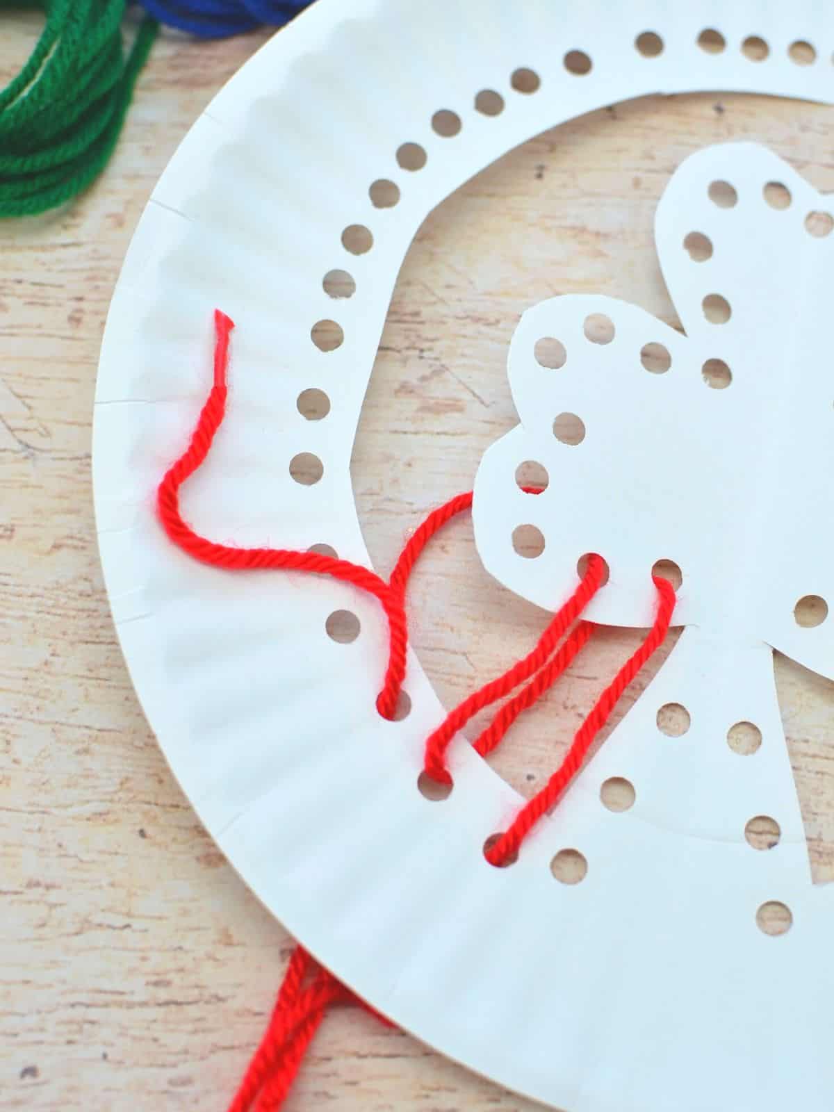 lacing red yarn through paper plate shamrock