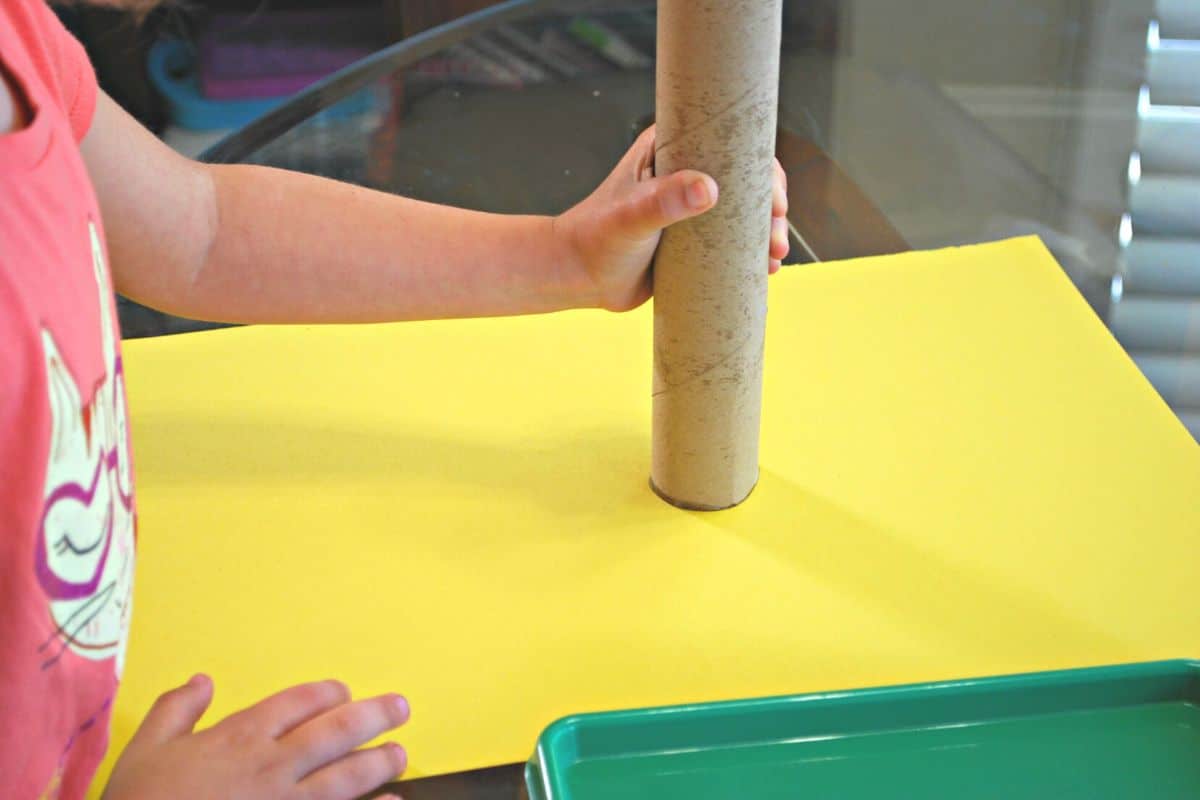 child stamping paper towel roll on yellow paper.