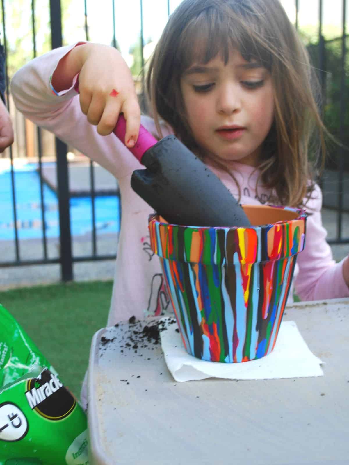 child placing dirt in a pour painted pot