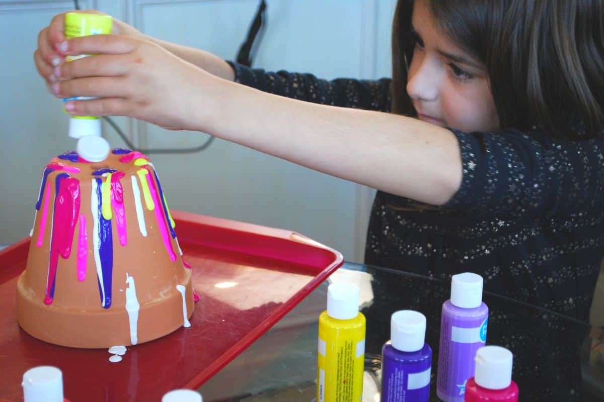 child squirting paint on flower pot.