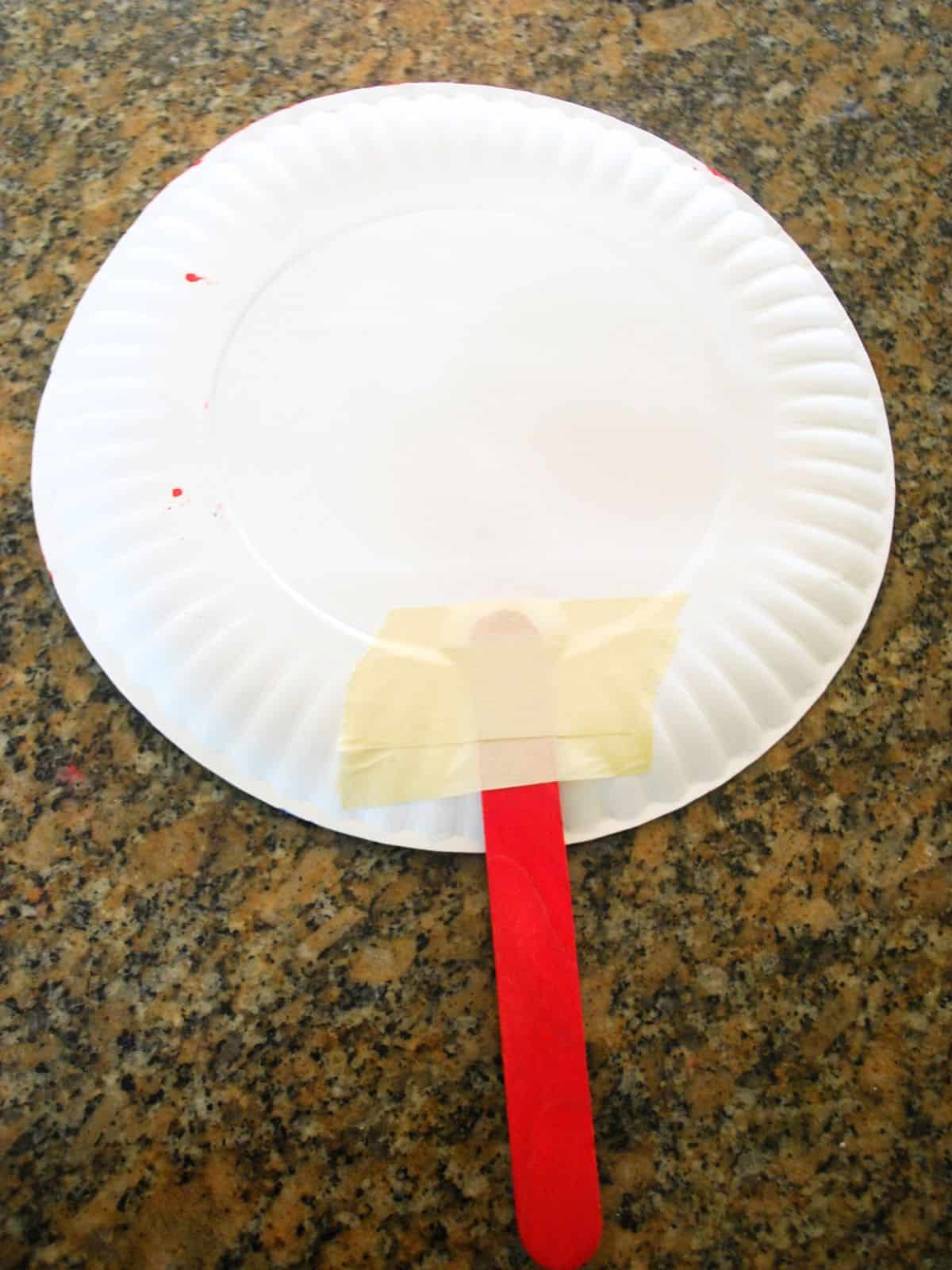 red popsicle stick taped to a white paper plate.