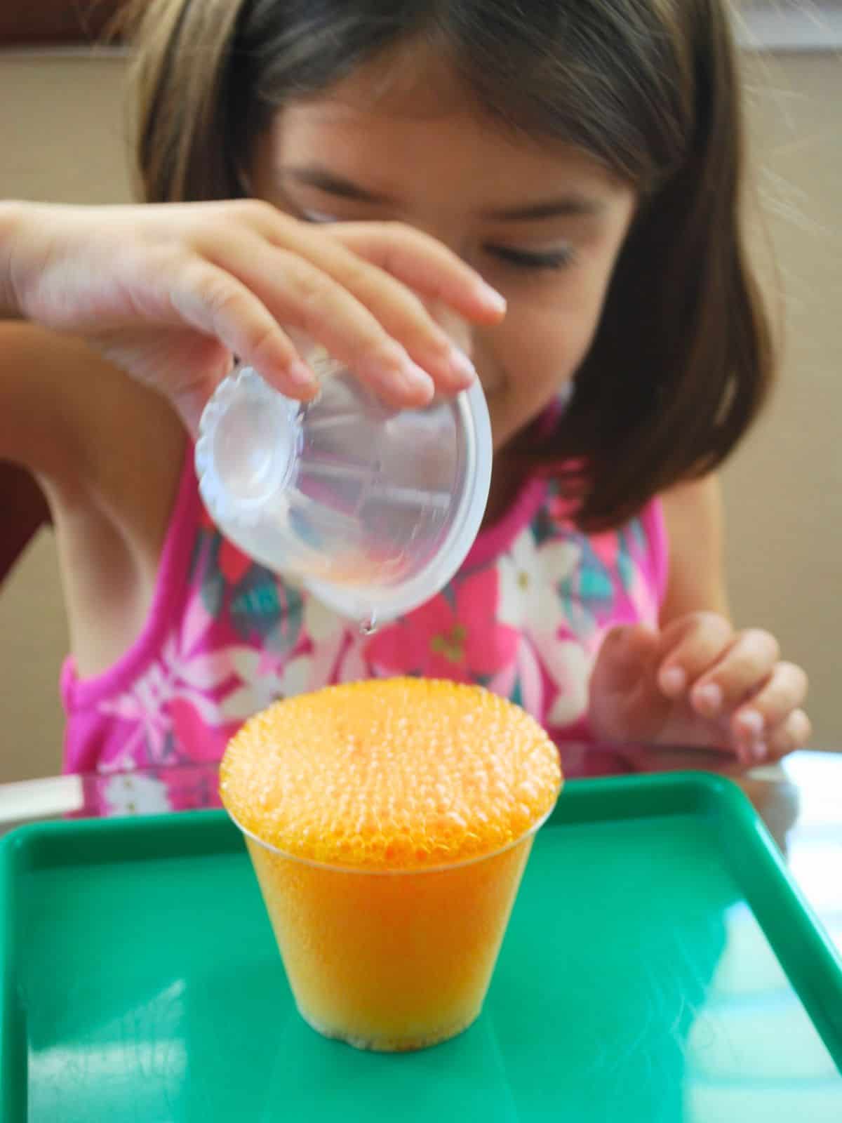 child pouring vinegar into cup of baking soda.