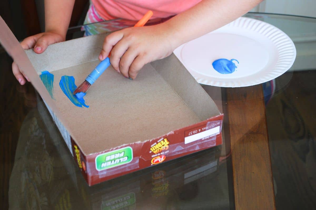 child painting the inside of a cereal box.