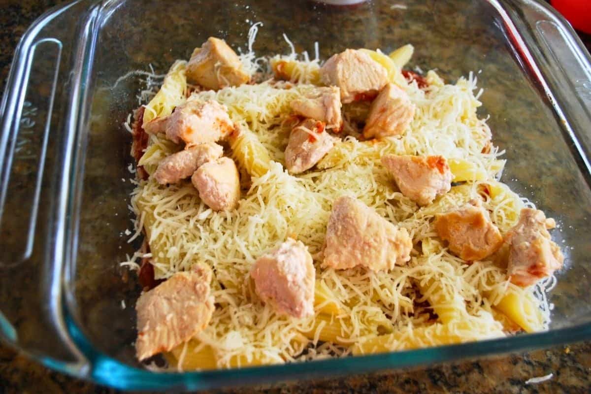 pasta chicken and shredded cheese in a casserole dish.