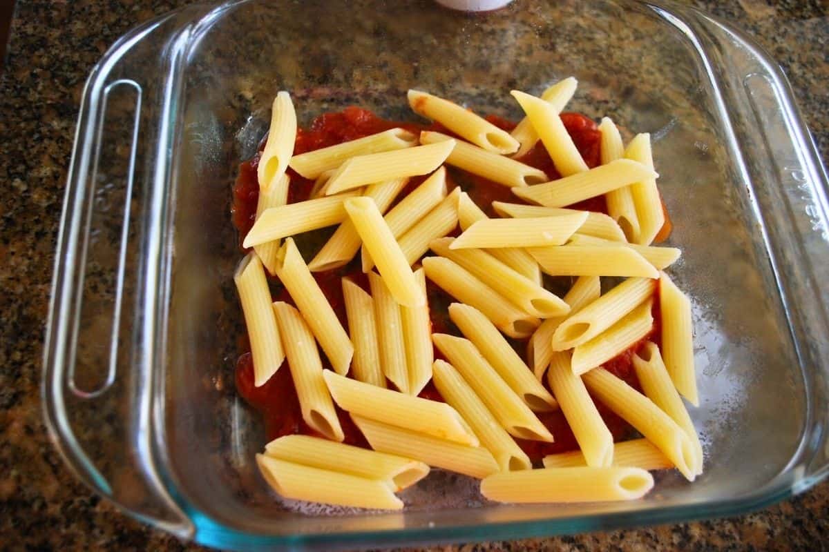 sauce and uncooked ziti in a baking dish.