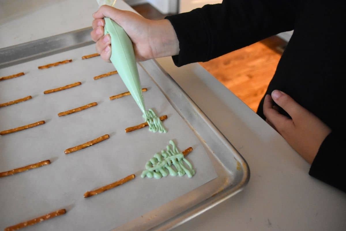 drizzling melted green chocolate on pretzel stick.