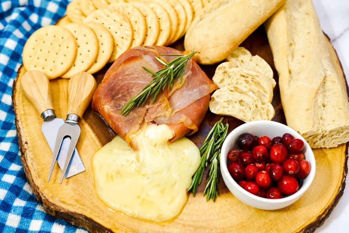 Prosciutto Wrapped Brie on platter with crackers and cranberries.